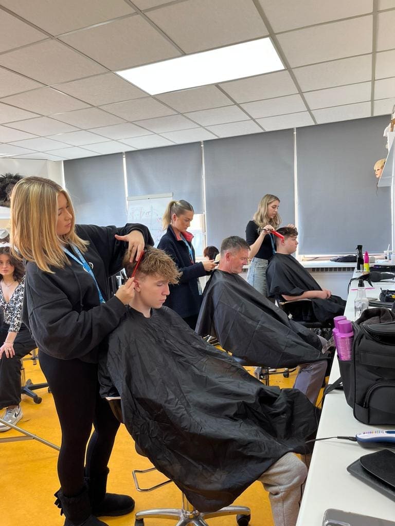 Brushstroke students practicing hairstyling on clients in a classroom setting